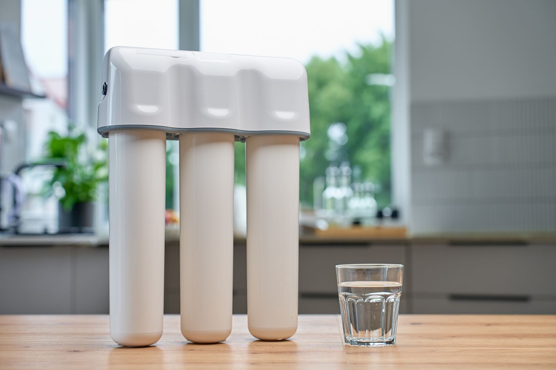 Three white water filter cartridges beside a glass of water on a kitchen counter
