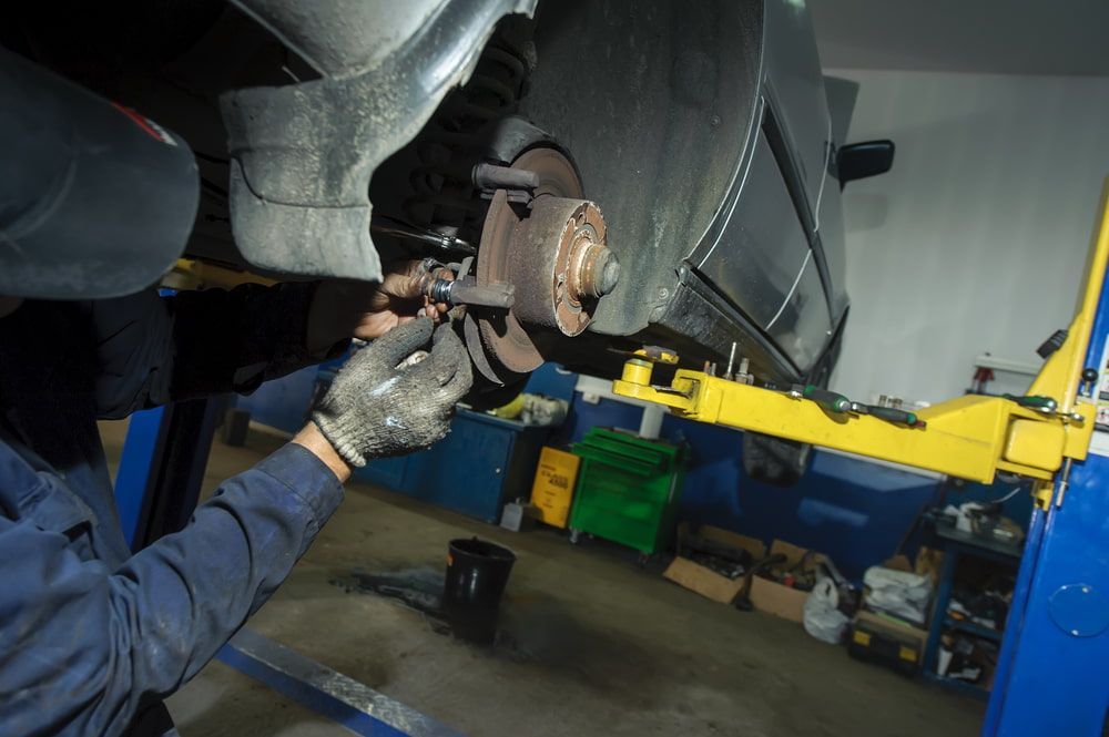 A Man Is Working on A Car on A Lift in A Garage — Coast Mechanical Services In Berkeley Vale, NSW
