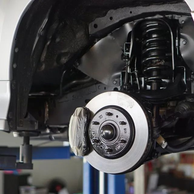 A Close up Of a Car 's Suspension and Brake System on A Lift — Coast Mechanical Services In Berkeley Vale, NSW