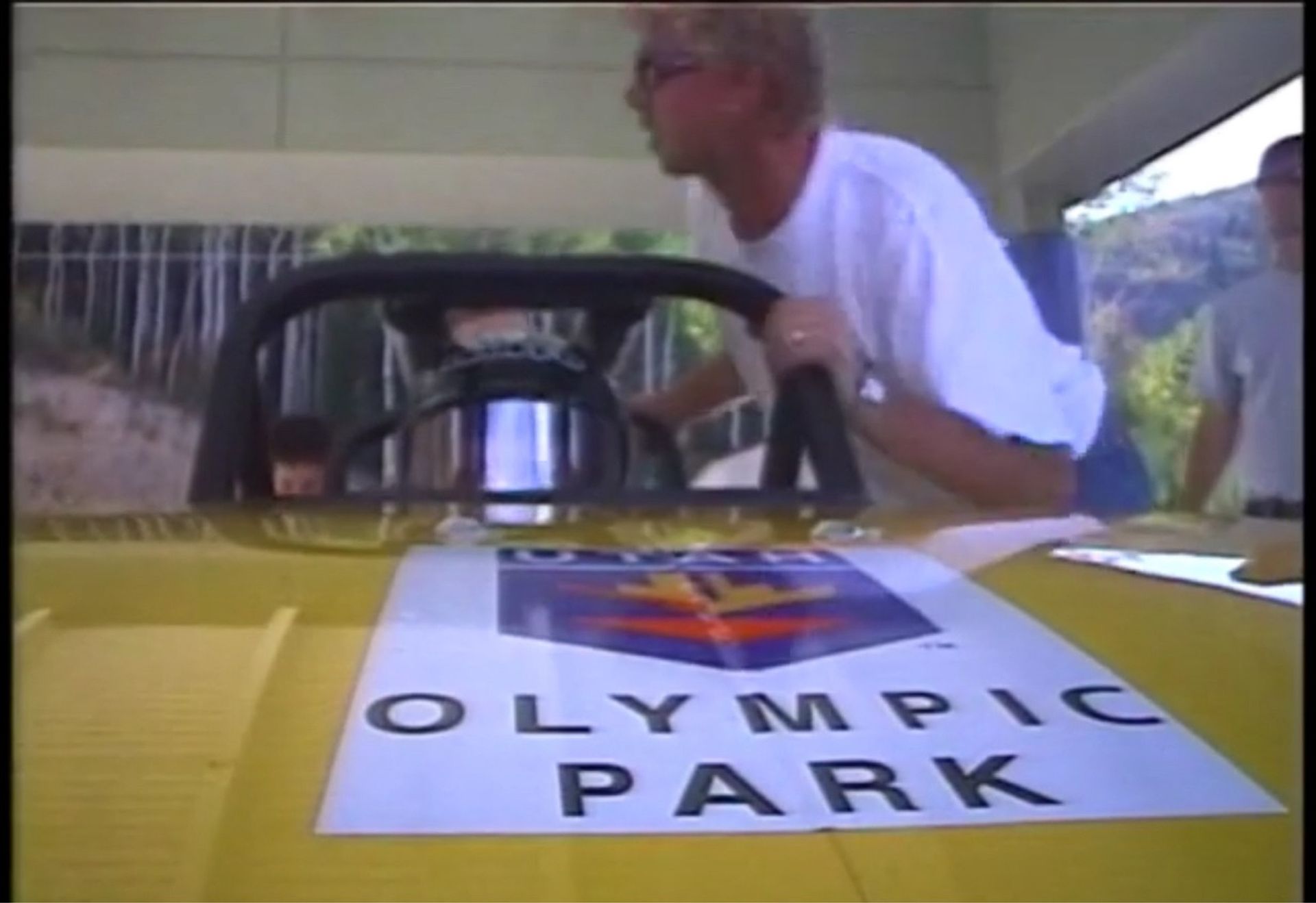 Tom Wright in a white shirt is standing next to a sign that says olympic park