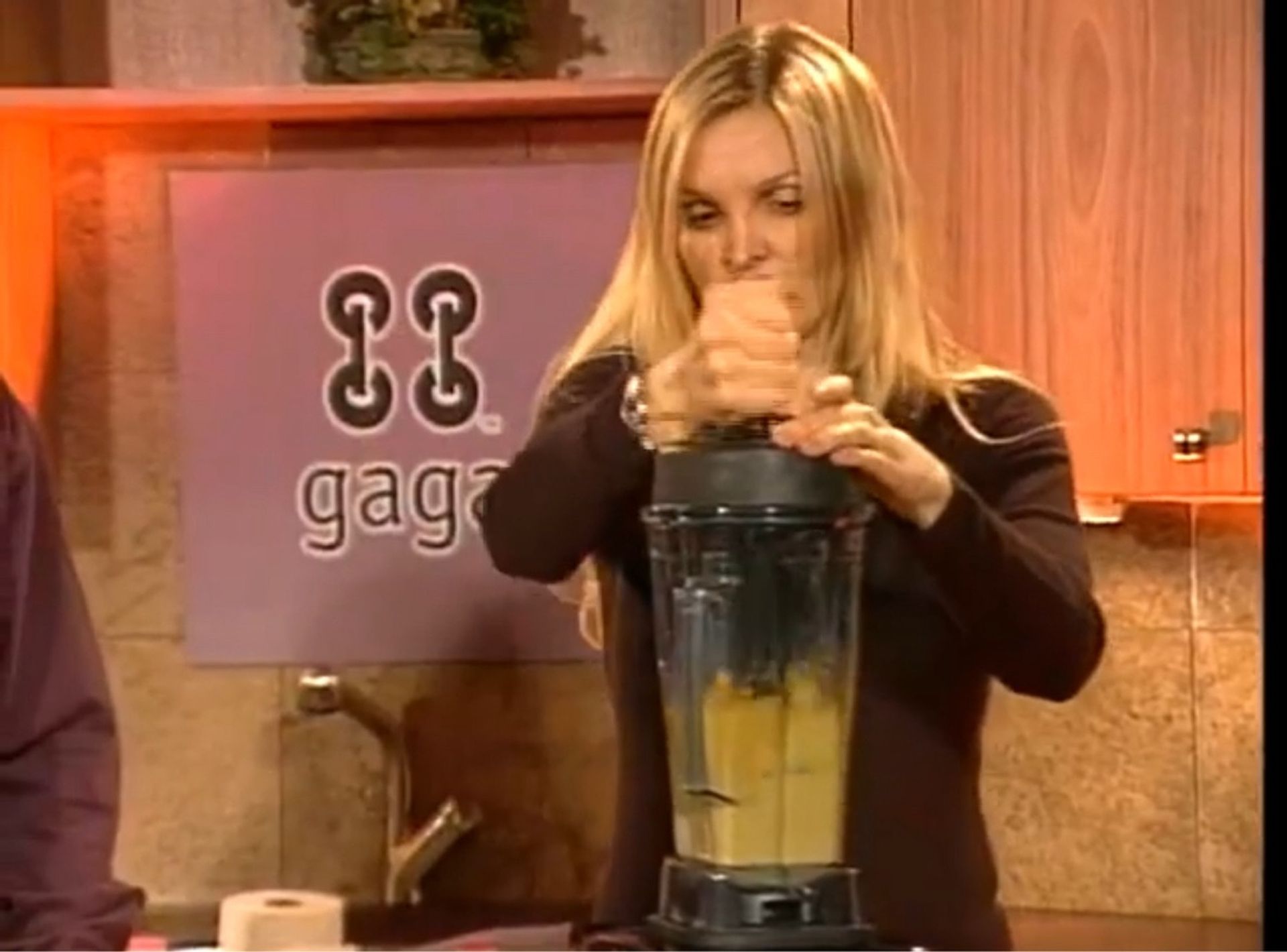 A woman is using a blender in front of a sign that says gaga