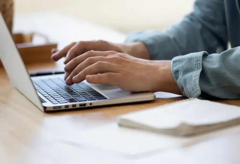 A person is typing on a laptop computer at a desk.