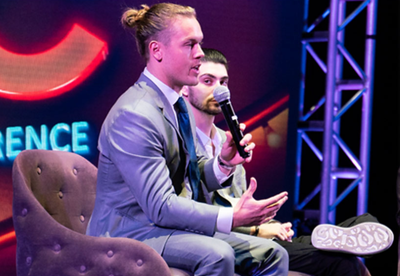 A man in a suit is holding a microphone in front of a sign that says conference