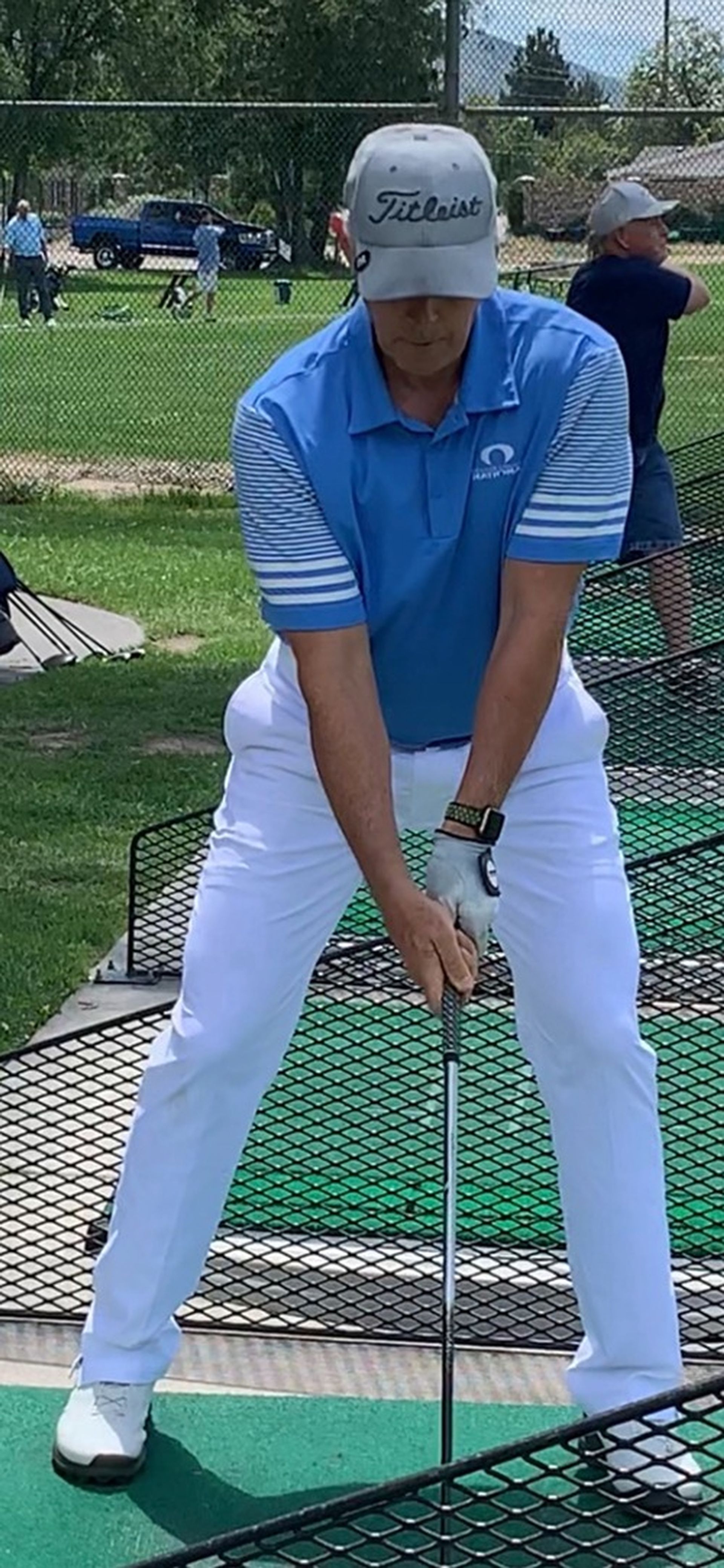 Tom Wright in a blue shirt and white pants is swinging a golf club on a golf course.