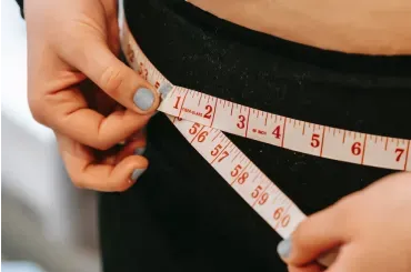 A woman is measuring her waist with a tape measure.