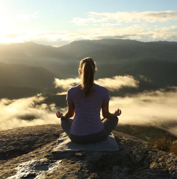 A woman sits in a lotus position on top of a mountain