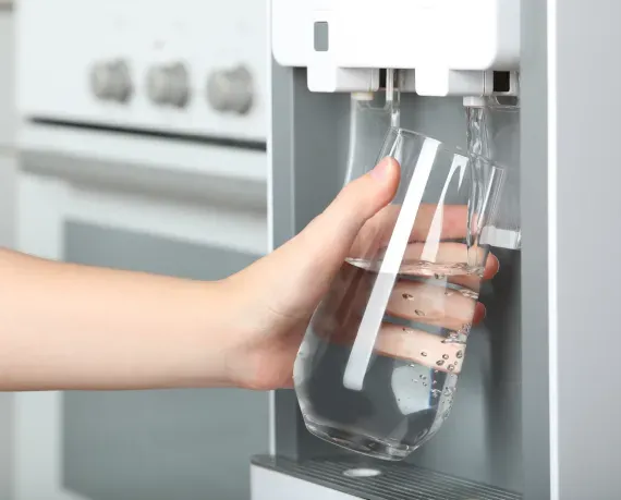 A person is pouring water into a glass from a water dispenser.