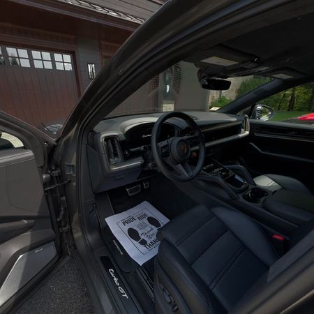 Car interior with driver’s door open, showing black seats, steering wheel, dashboard, and a paper on the floor.