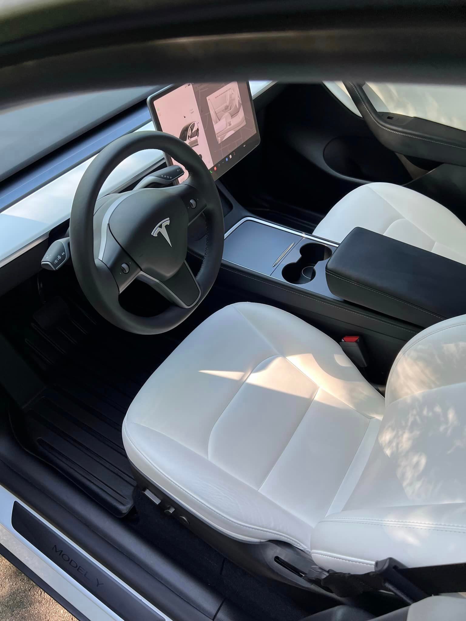 Tesla car interior with white seats, black steering wheel, center console, and dashboard screen