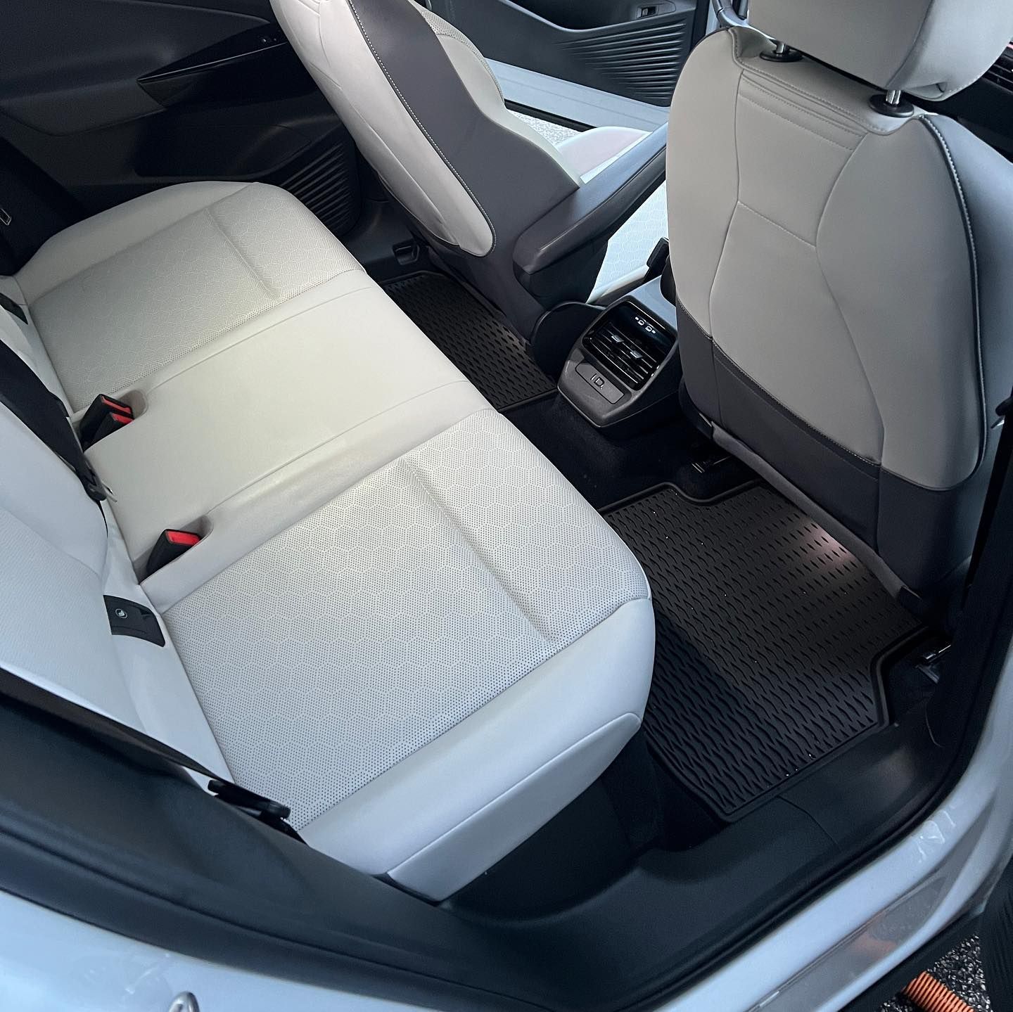 Rear car seats with light gray upholstery and black floor mats, viewed from the open door.