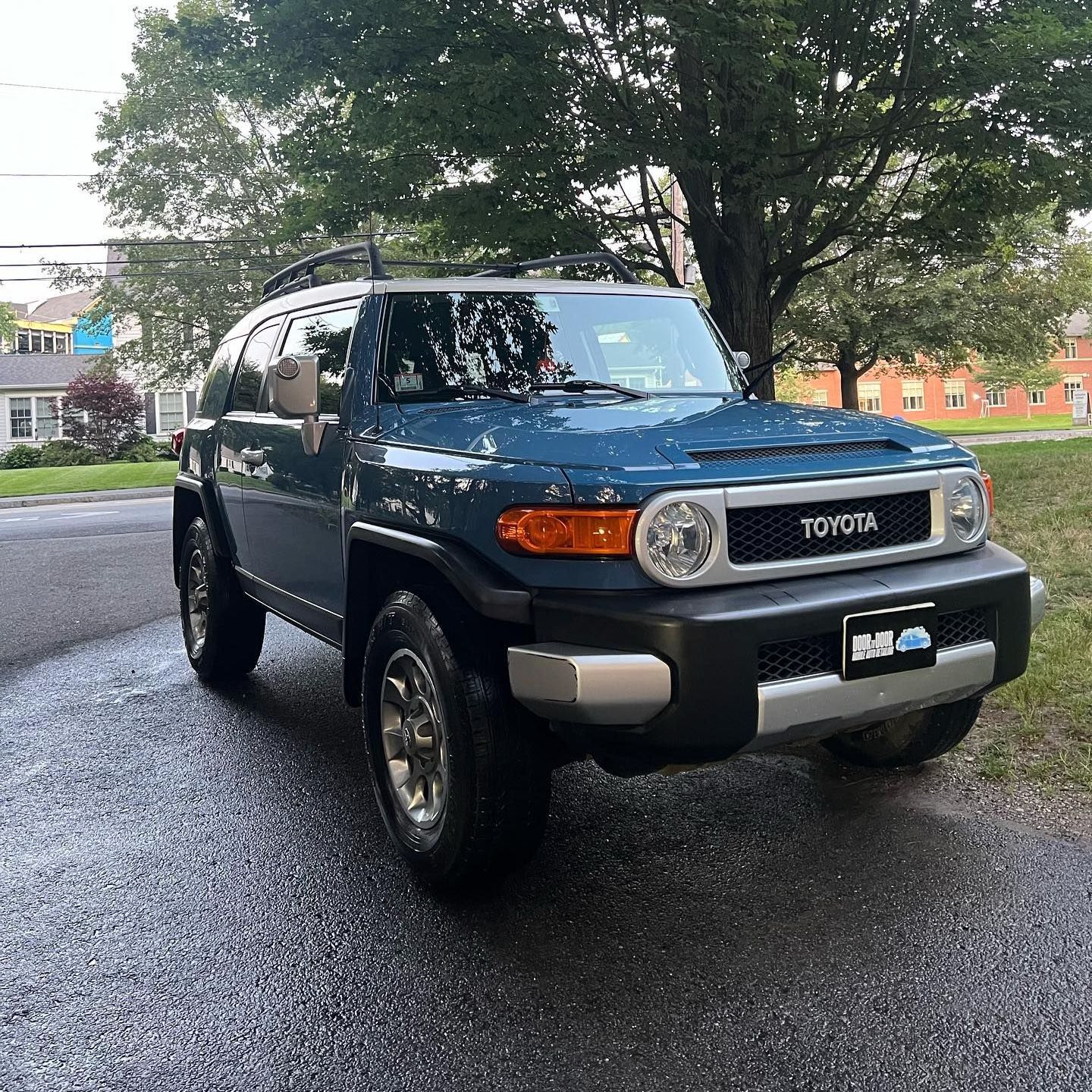 Blue Toyota SUV parked on a wet road under trees in a residential area