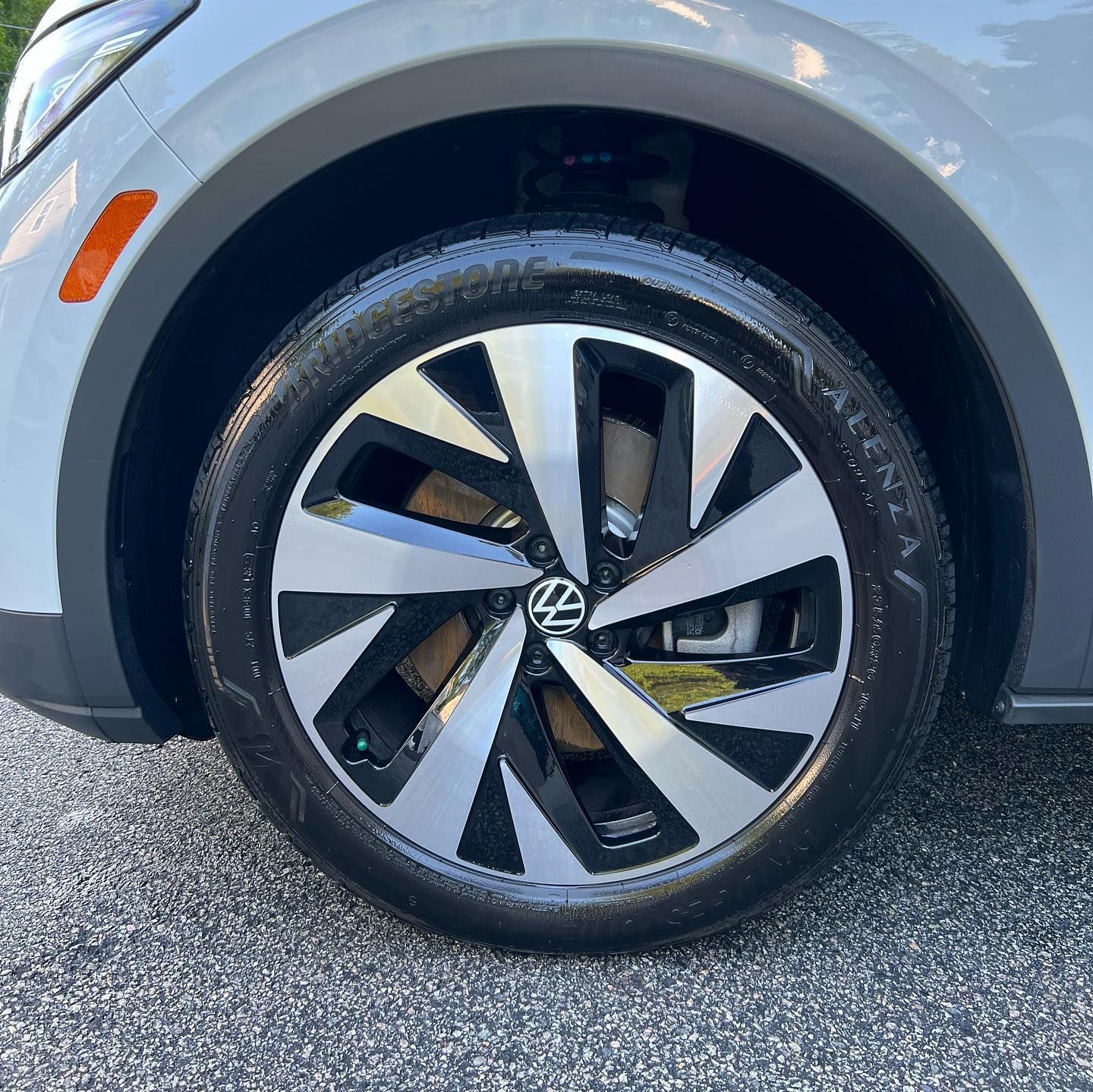 Close-up of a silver car’s front wheel with a black-and-silver alloy rim and Volkswagen logo.