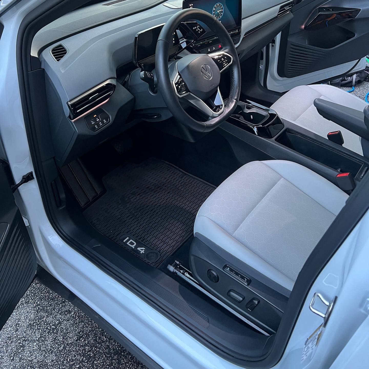 Open car door showing a light gray modern vehicle interior with steering wheel, seat, and floor mat