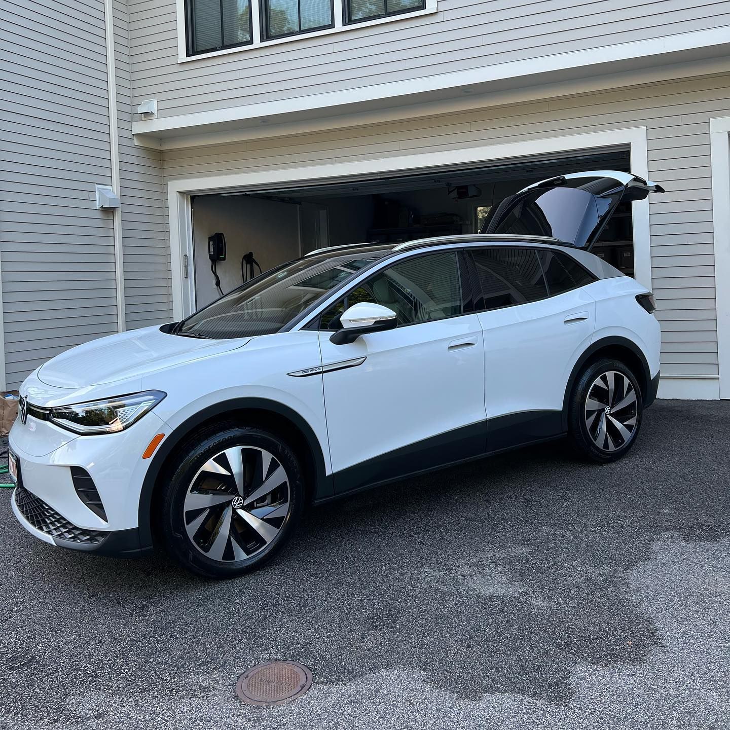 White SUV parked in a driveway beside a garage in front of a house.