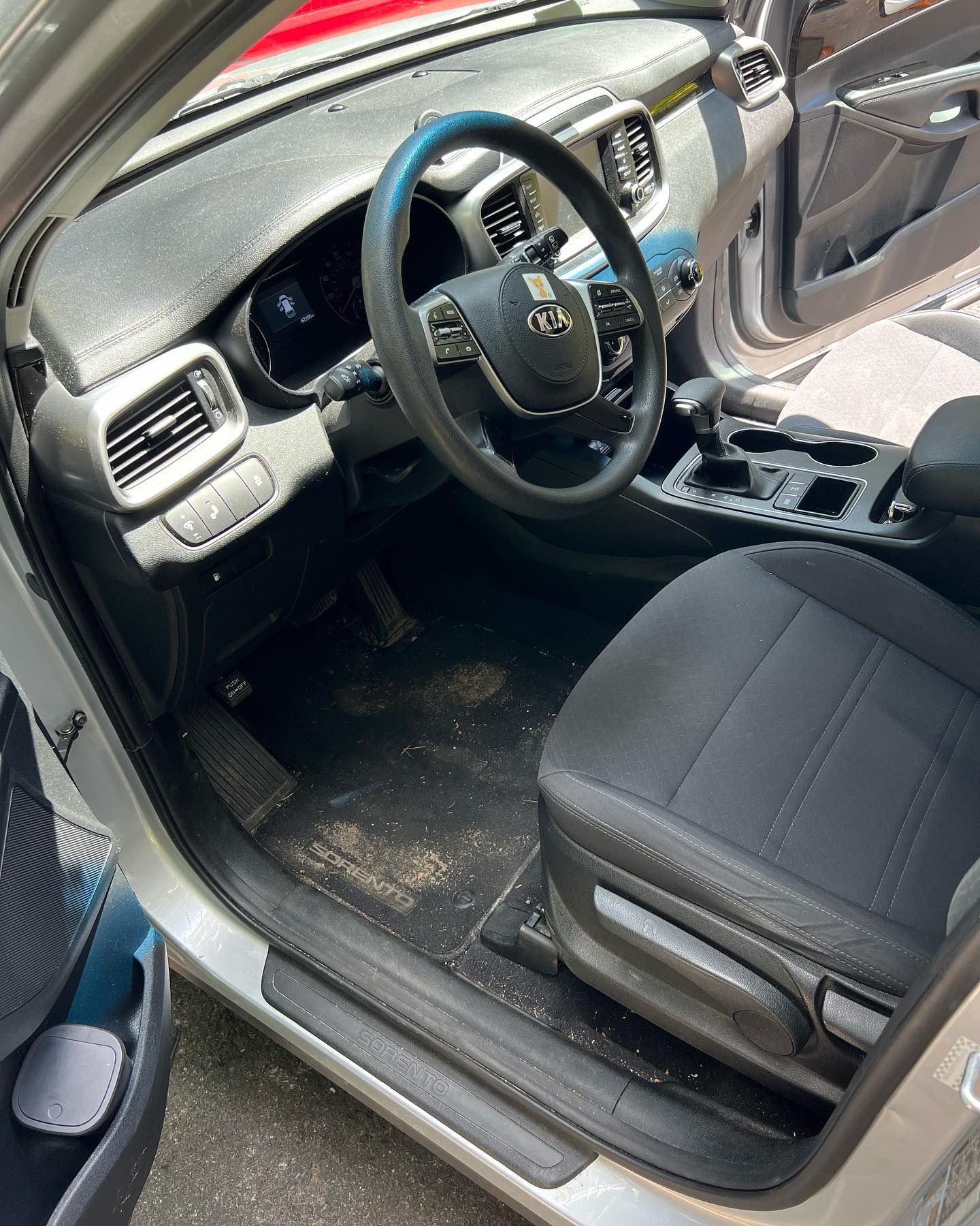 Car interior with black seats, steering wheel, and center console, viewed through an open driver’s door
