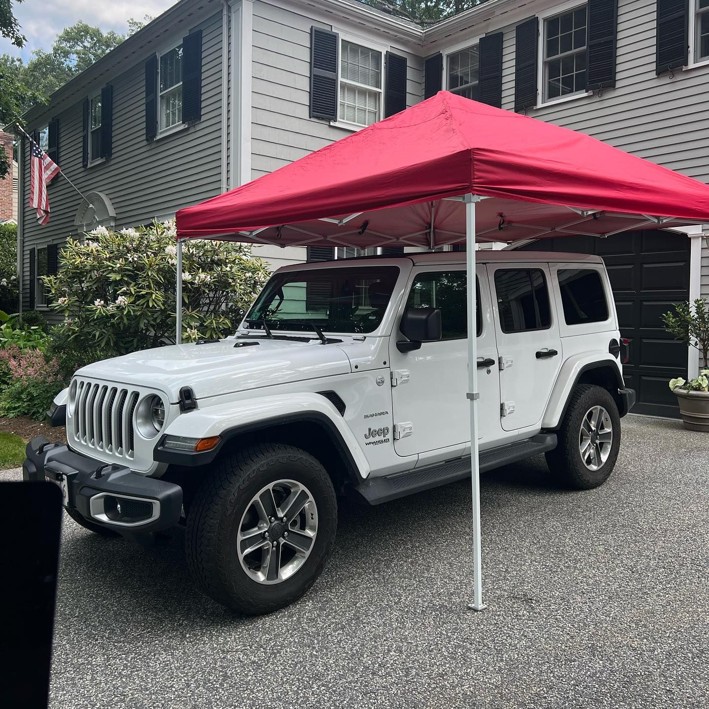 White Jeep Wrangler under a bright pink canopy in a driveway beside a house