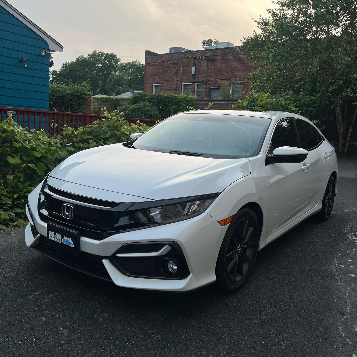 White Honda Civic parked on a wet driveway beside houses at dusk