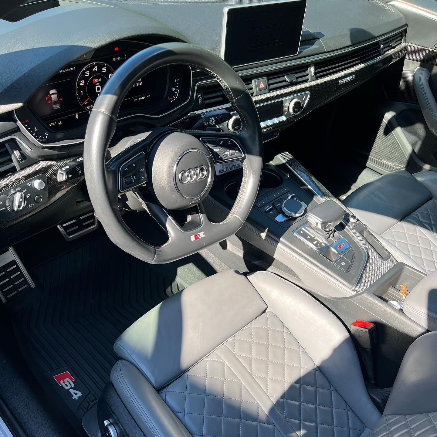 Luxurious car interior with gray quilted seats, Audi steering wheel, and center console.