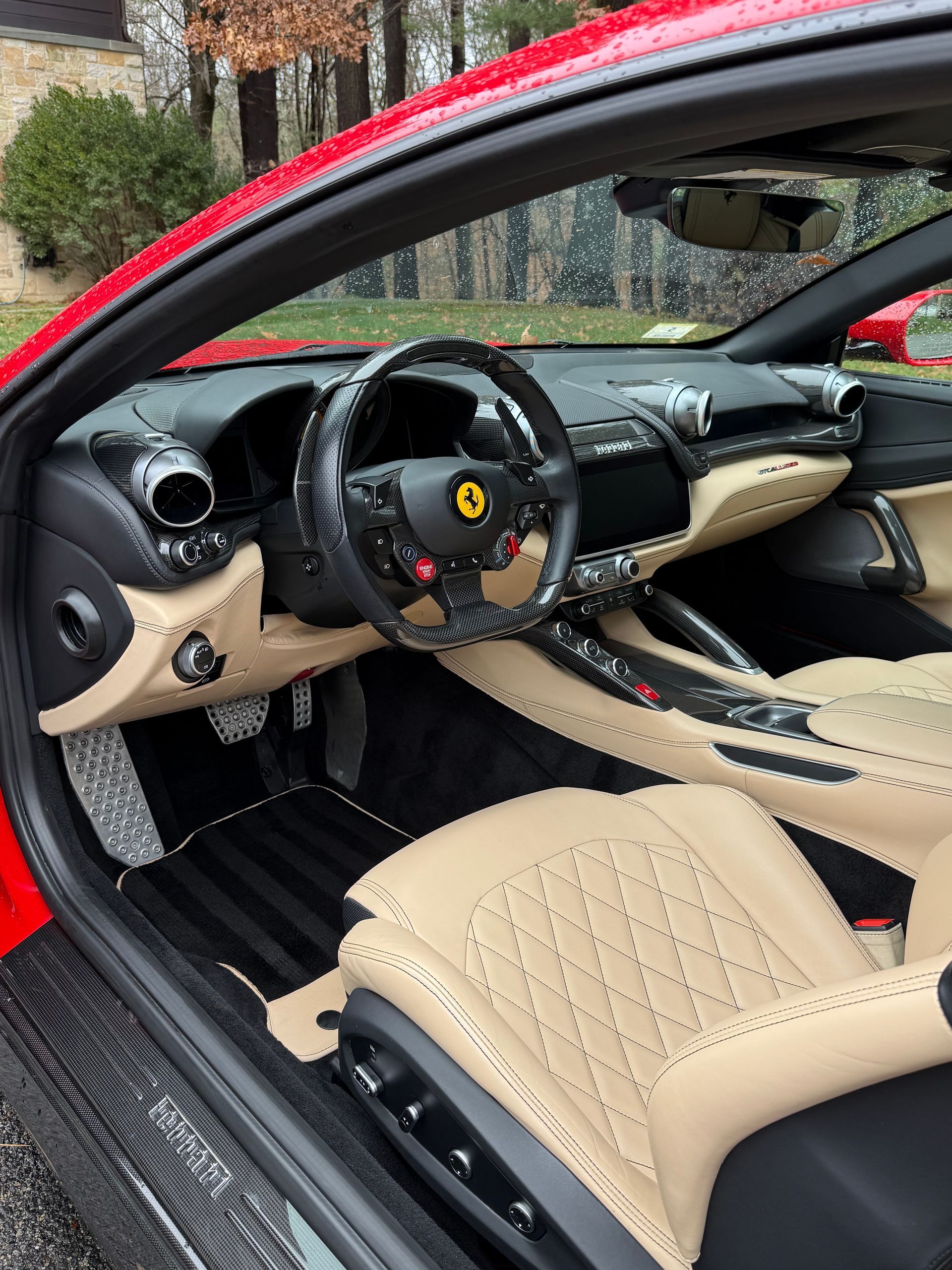 Luxury sports car interior with tan leather seats, black dashboard, and red exterior door frame open