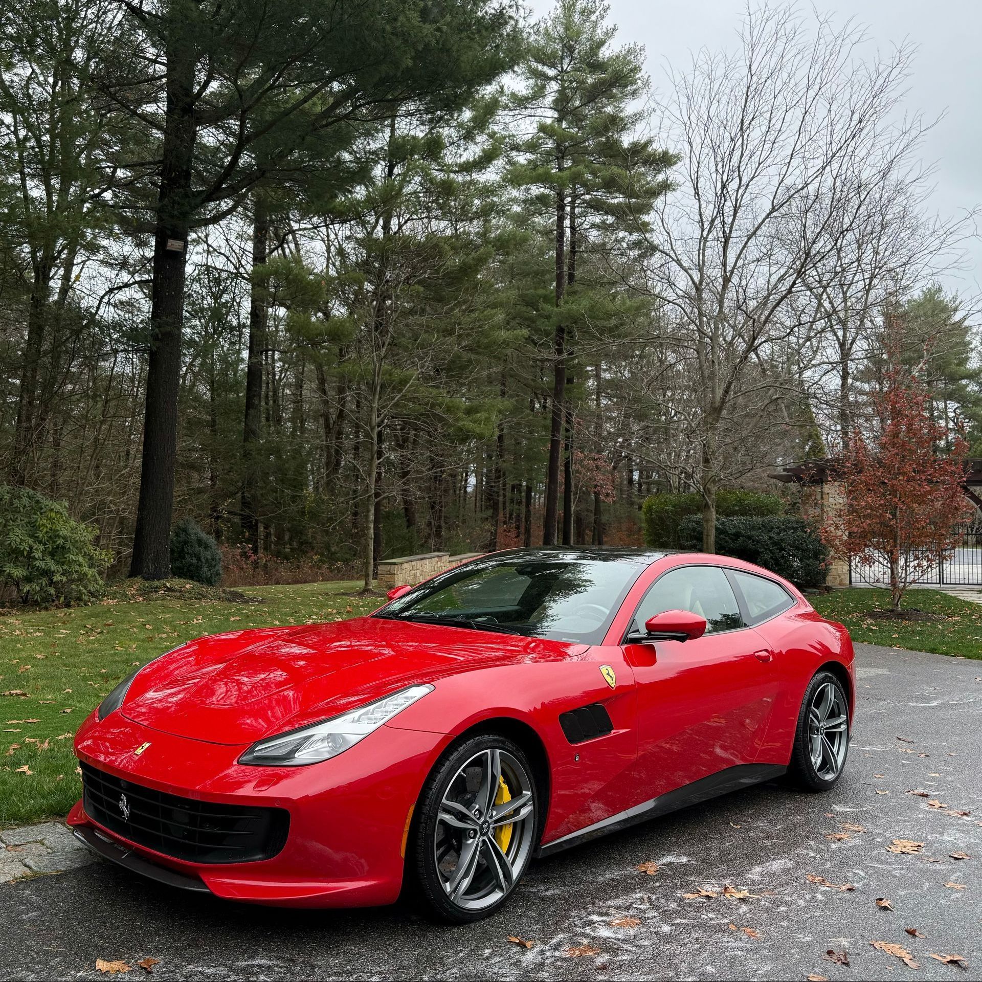 Red sports car parked on a wet driveway beside trees and a house
