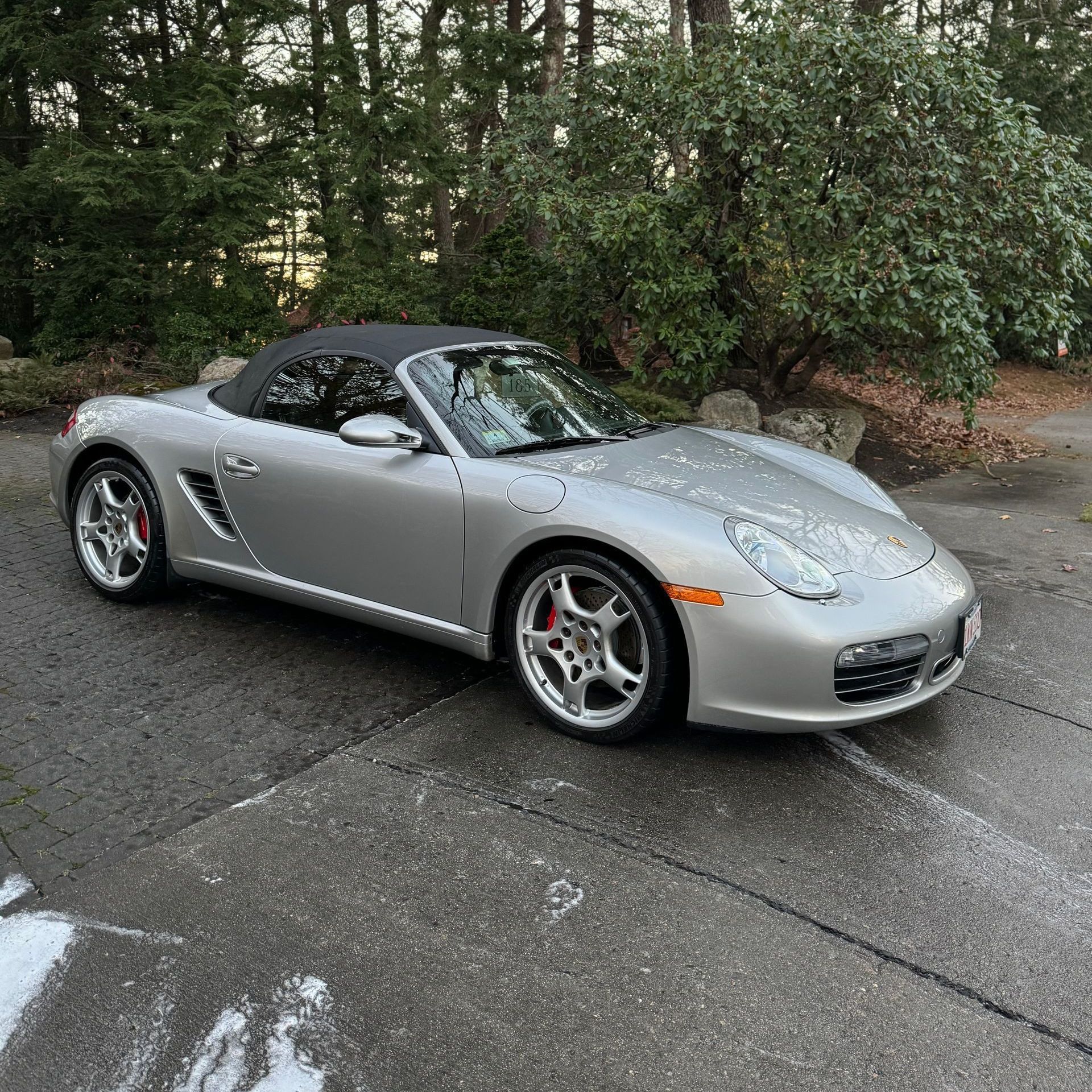 Silver convertible sports car parked on a wet driveway beside trees