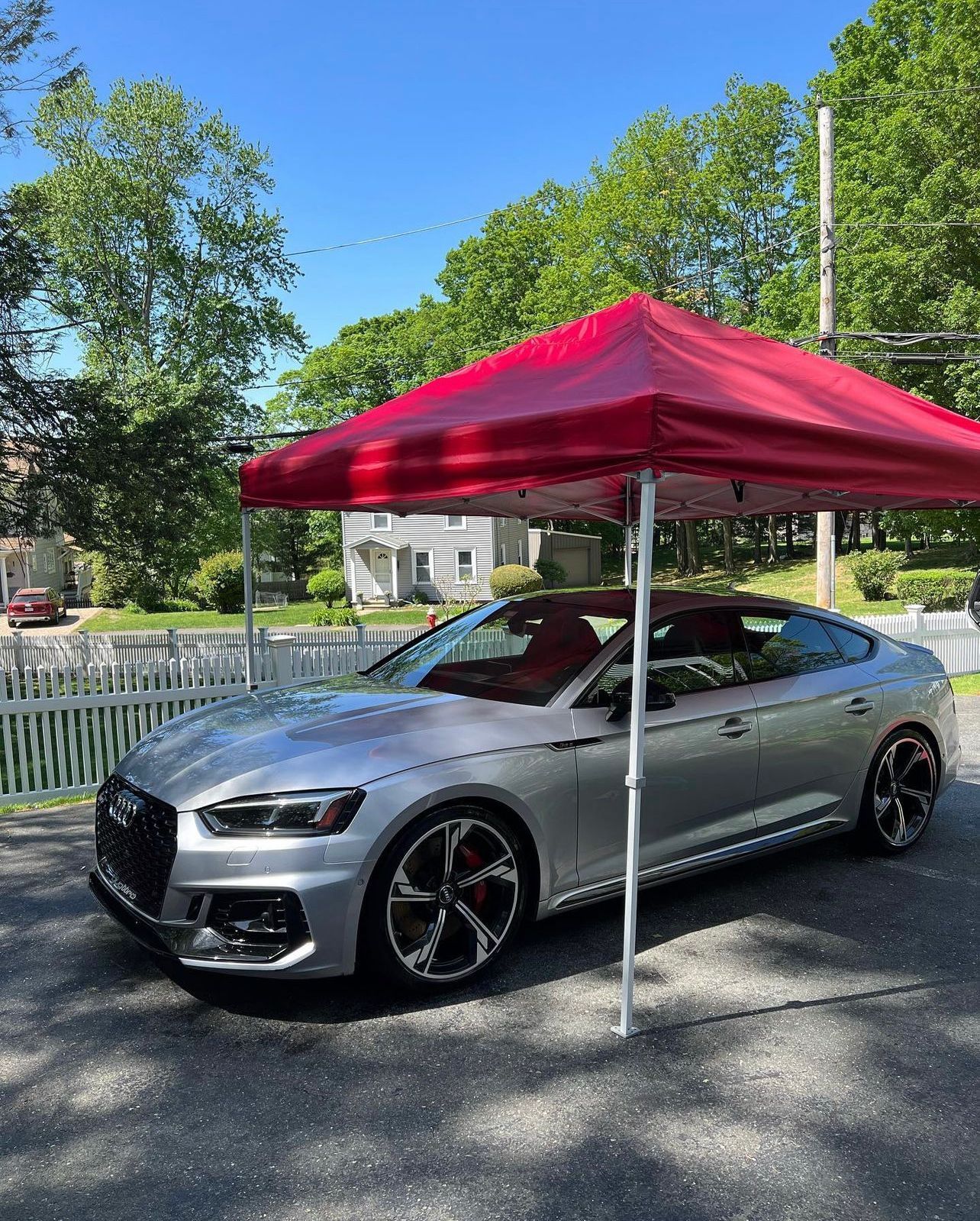 Silver sports coupe parked under a red canopy in a sunny outdoor lot