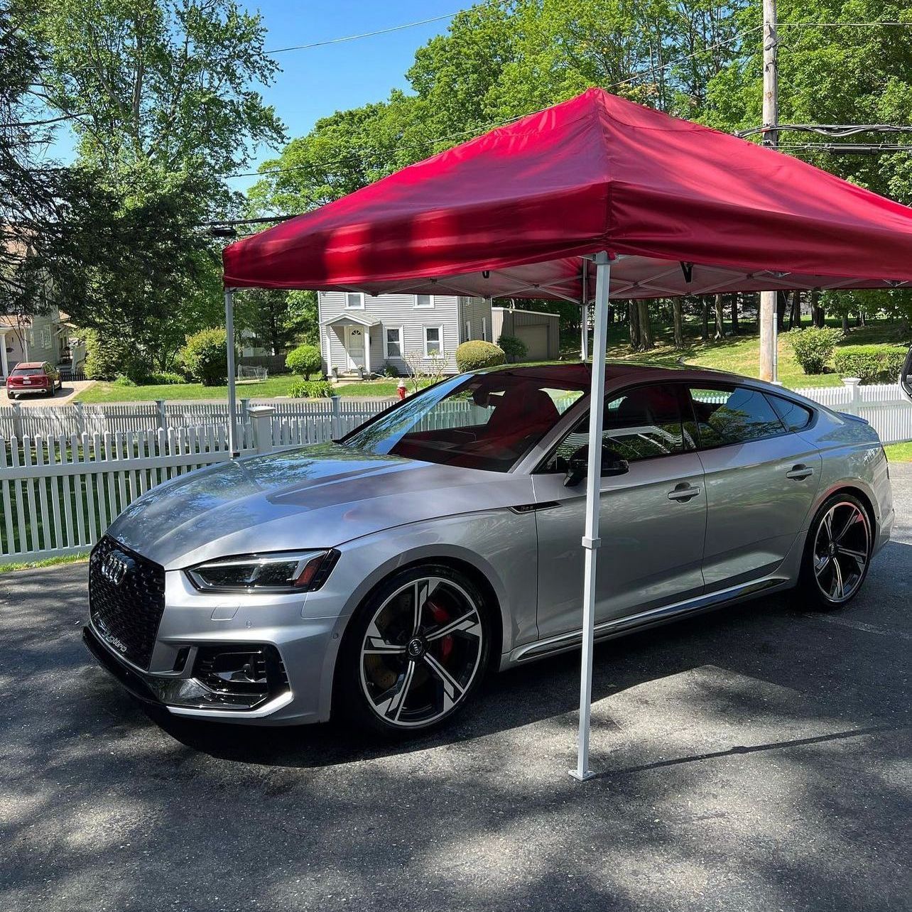 Silver coupe parked under a red canopy on a sunny residential street.
