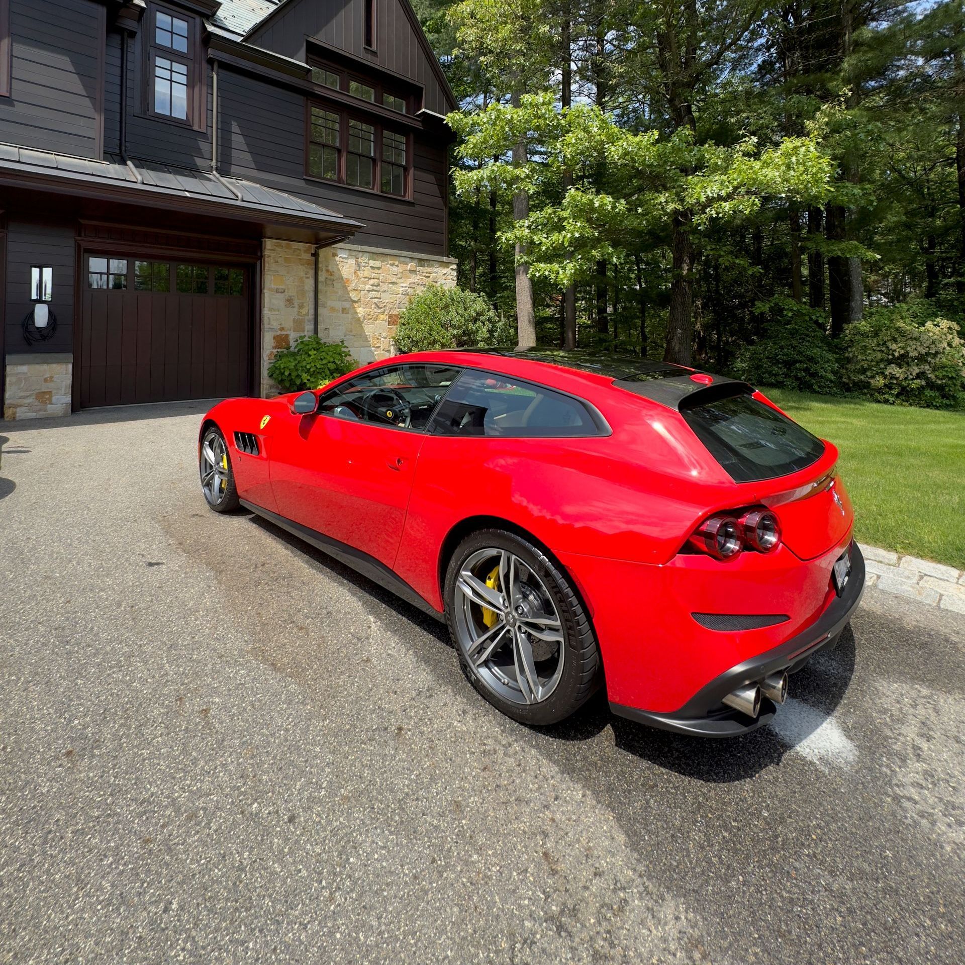 Red sports car parked in a driveway beside a house and wooded yard
