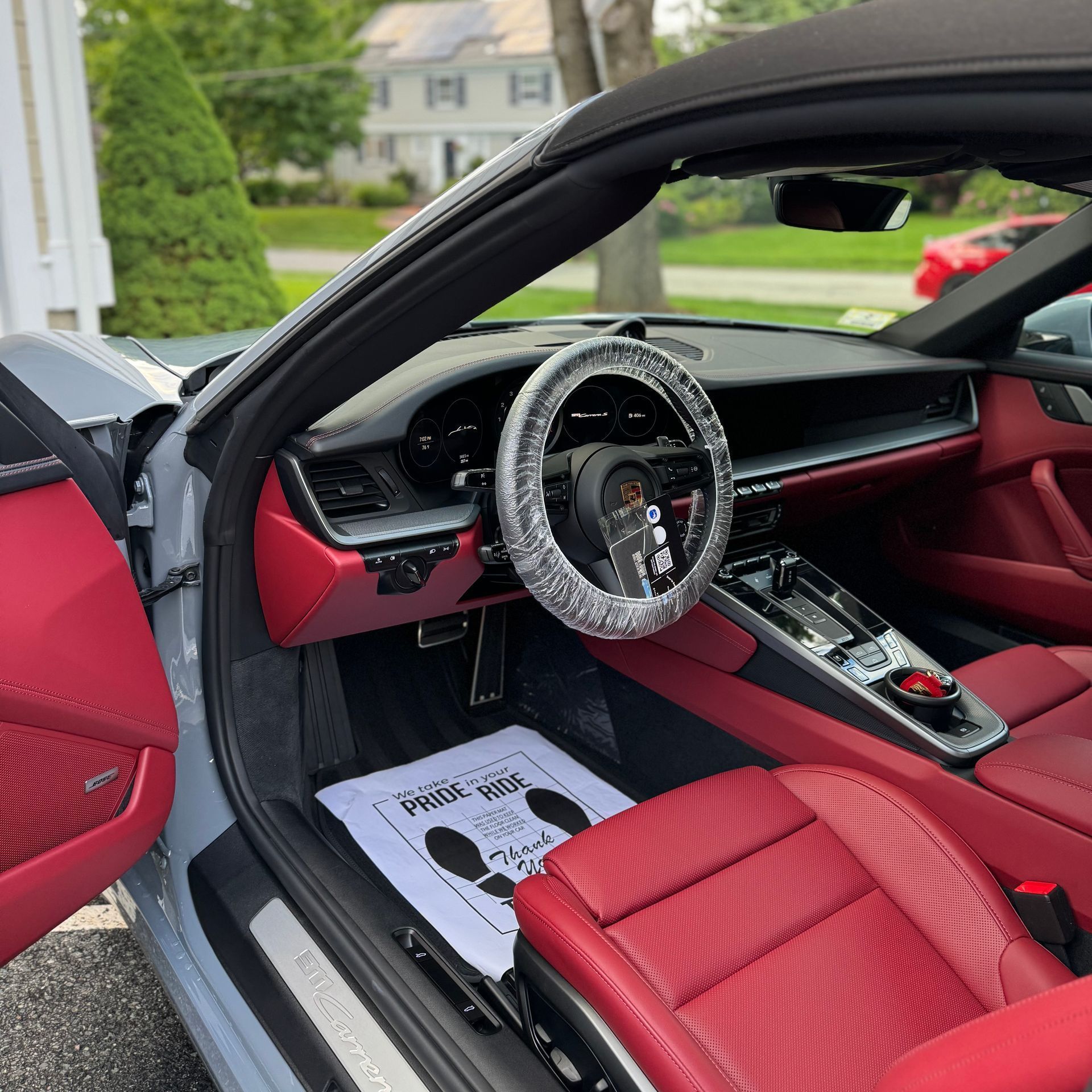 Red sports car interior with red seats and steering wheel cover, door open, parked outside rumah.