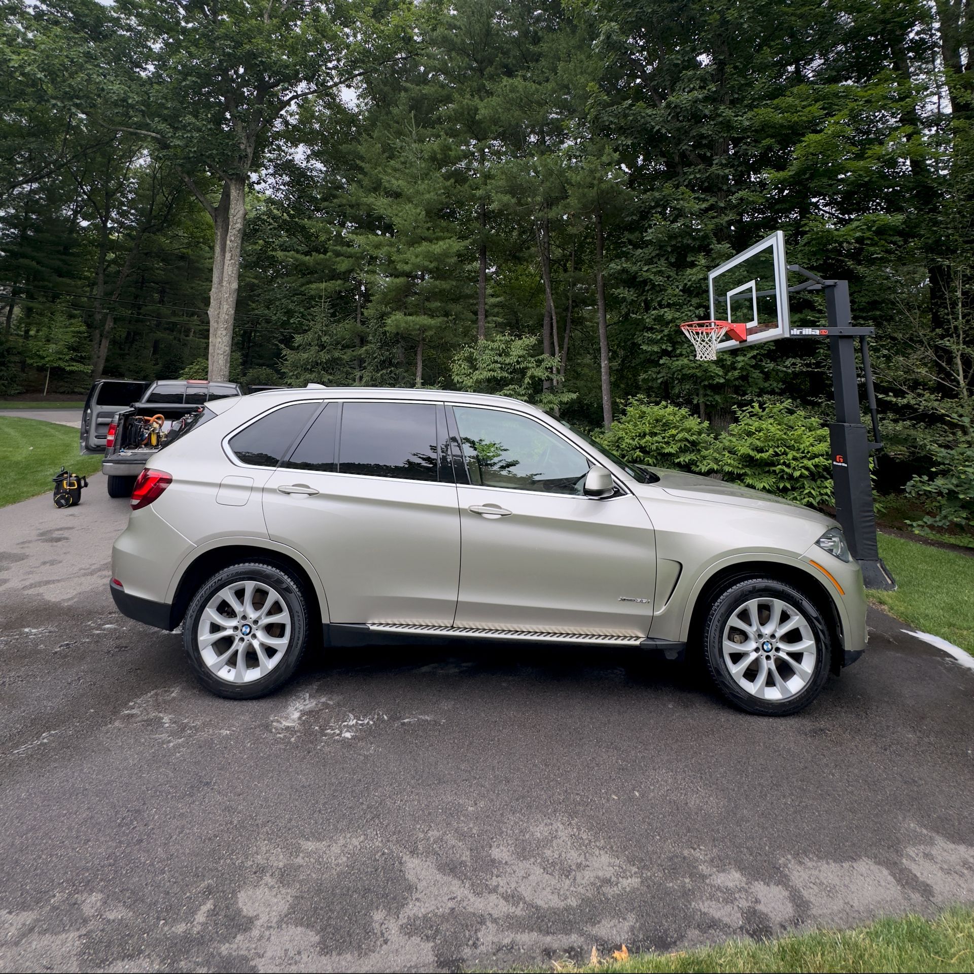 Silver SUV parked beside a driveway basketball hoop in a wooded area