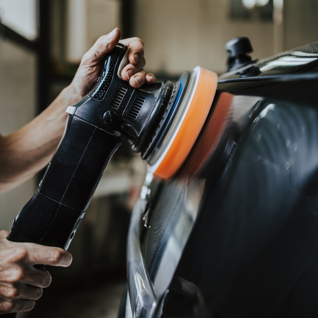 Person polishing a black car with a power buffer and orange pad