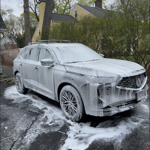 White SUV covered in foam during a car wash on a snowy driveway
