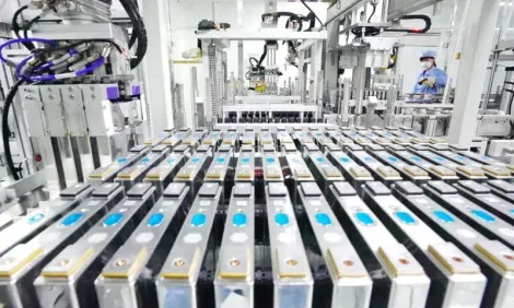 File di celle di batteria su una linea di produzione automatizzata in fabbrica, con apparecchiature robotiche in alto.