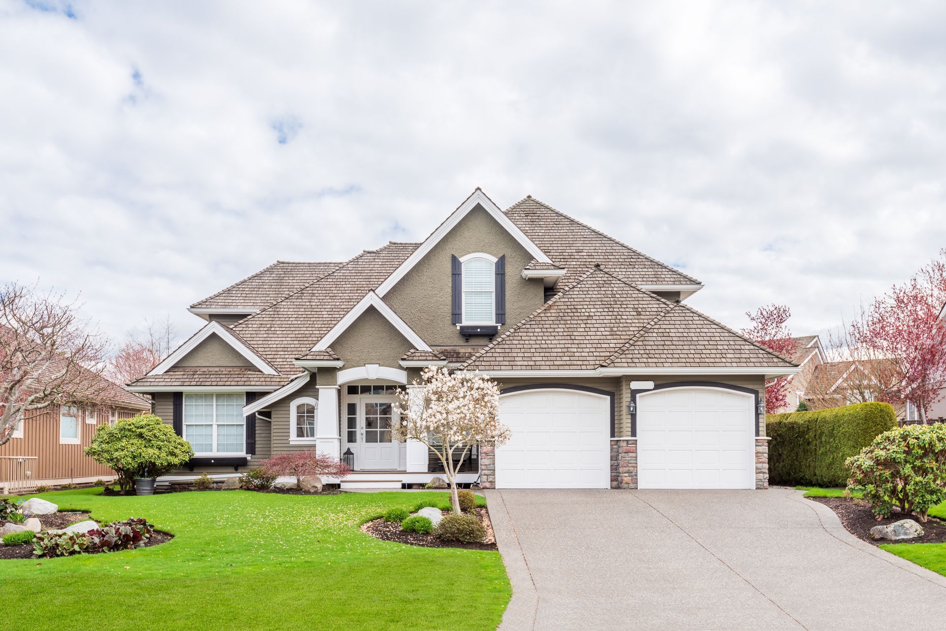 A large house with two garage doors and a driveway in front of it.