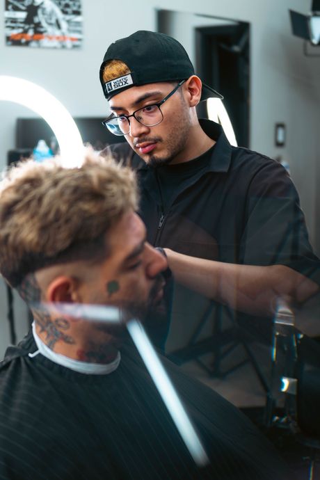 A barber carefully styles a client's hair in a professional, brightly lit salon setting. The Studio Barbershop