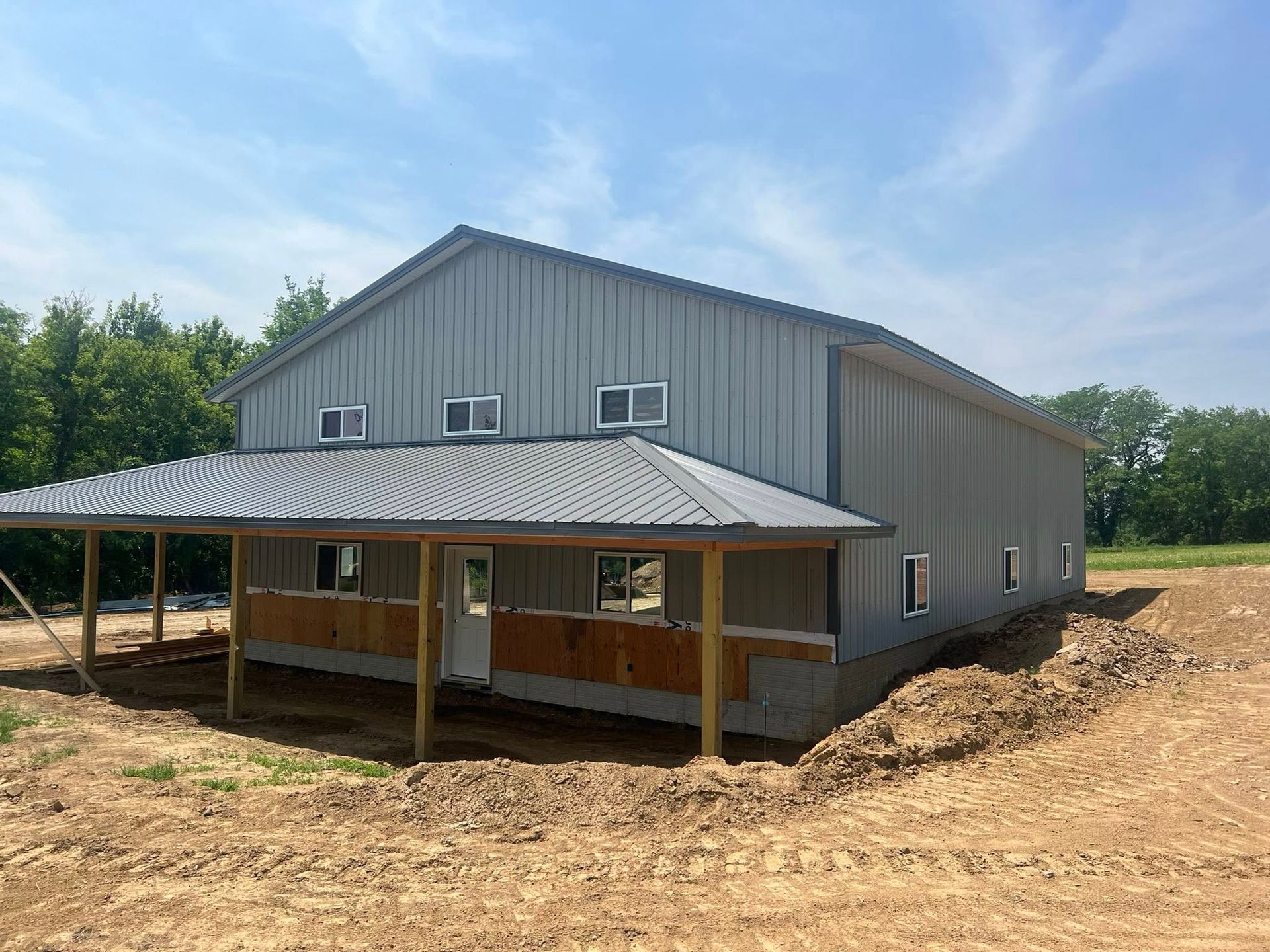 A gray post frame building with a porch and a blue sky in the background
