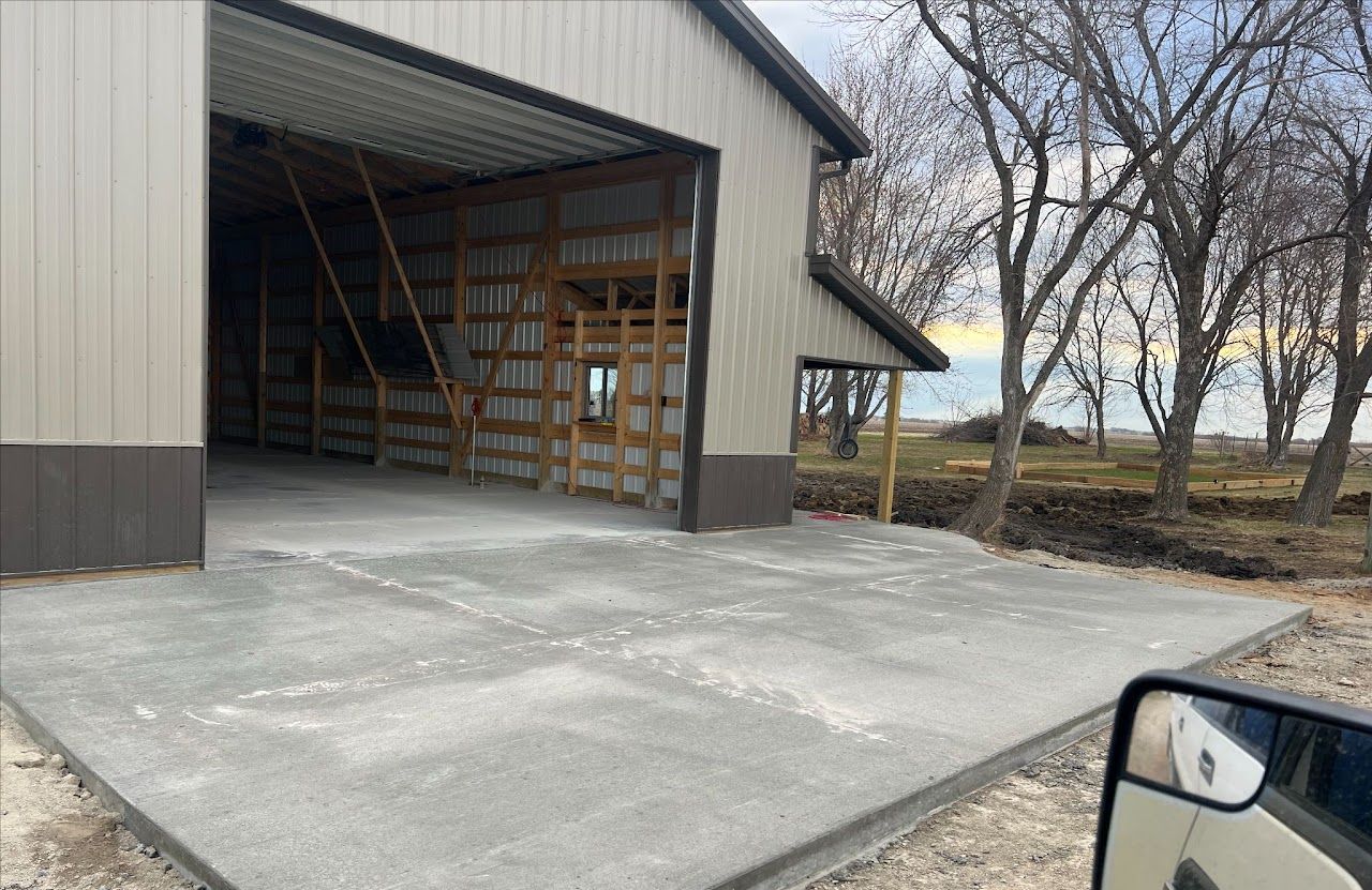 A car is parked in front of a pole barn with a large garage door.