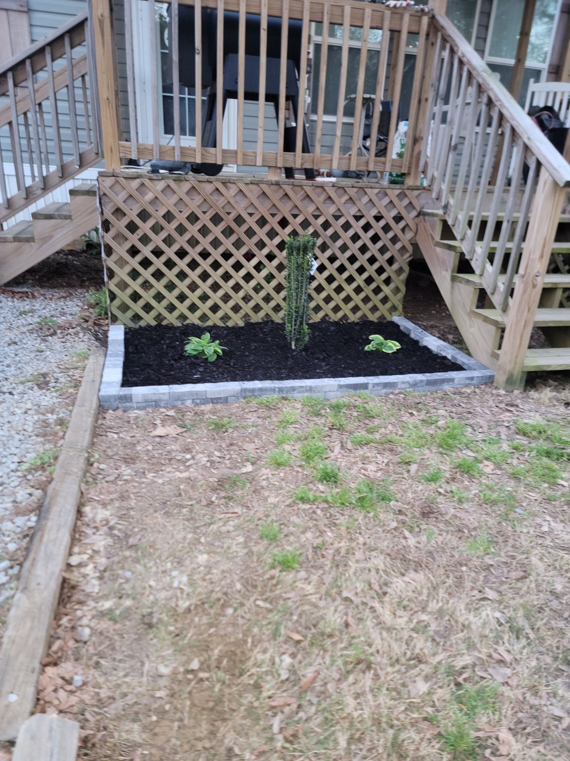 Backyard deck stairs with lattice skirting and a small mulched planting bed below