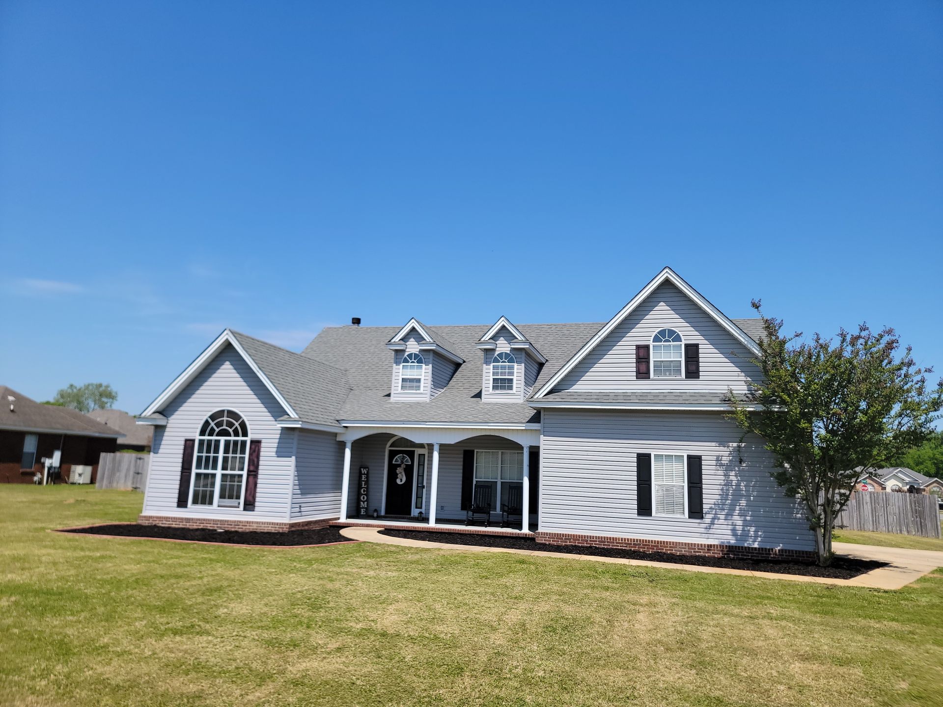 Suburban white house with gray roof and large front lawn under a clear blue sky
