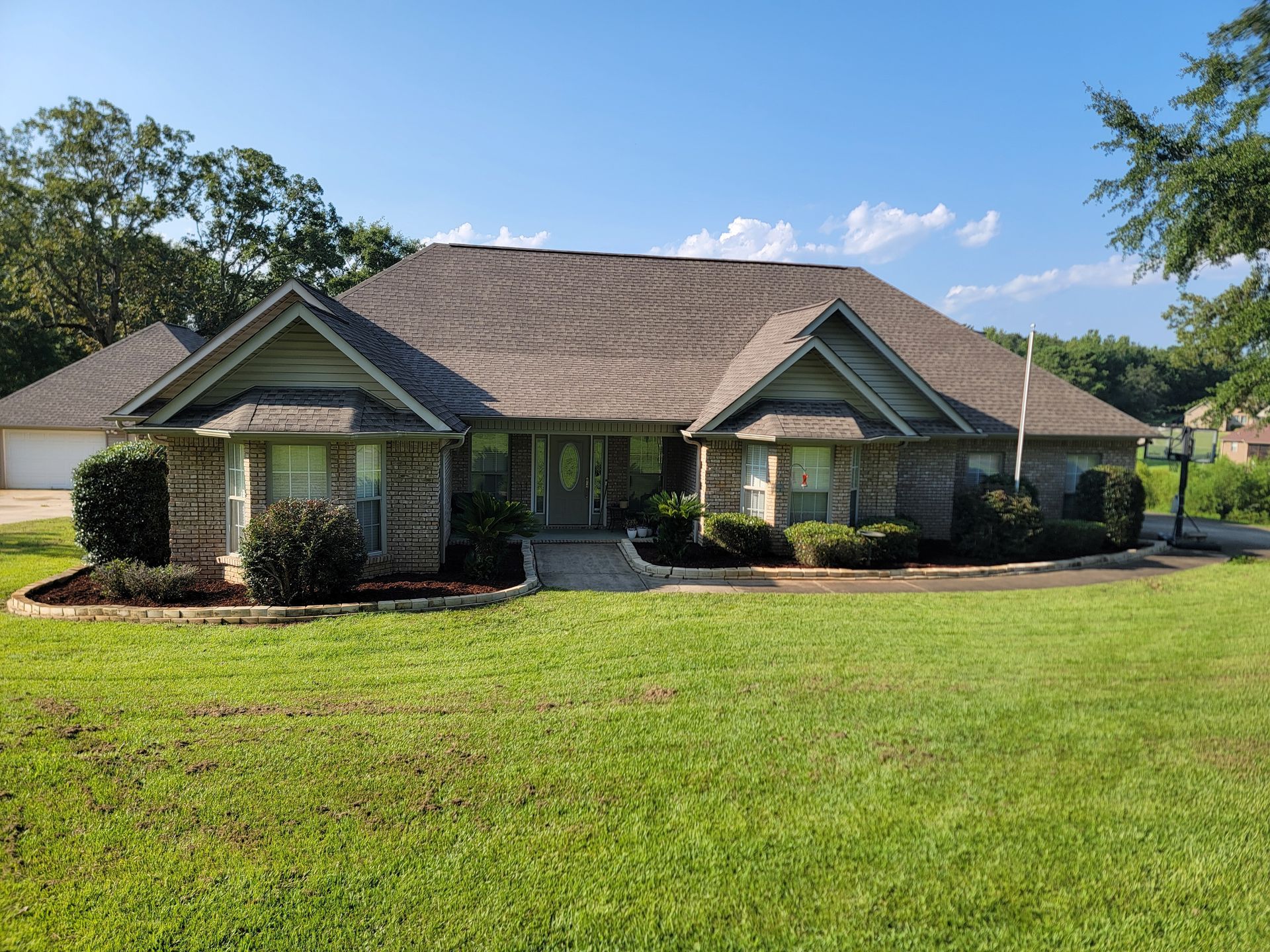 Single-story brick house with a large green lawn and clear blue sky