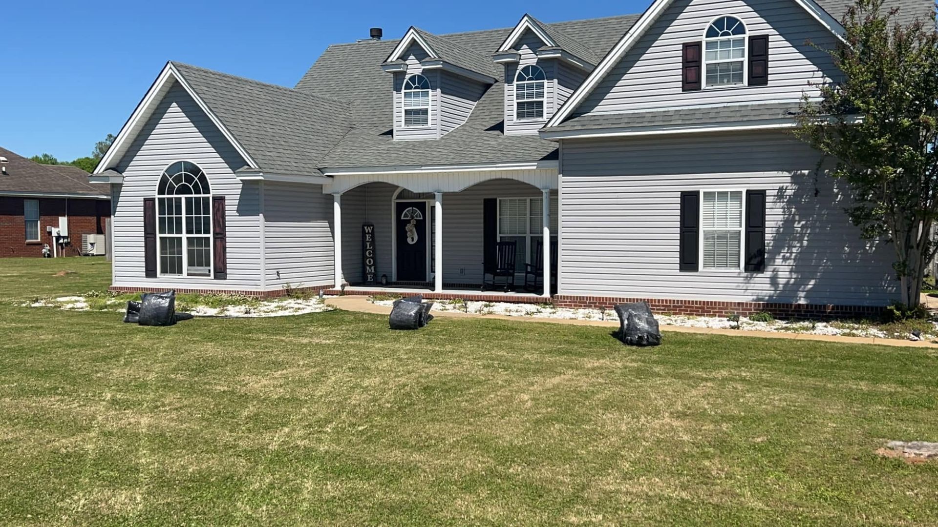 White suburban house with gray roof and arched windows, set behind a mowed lawn on a sunny day