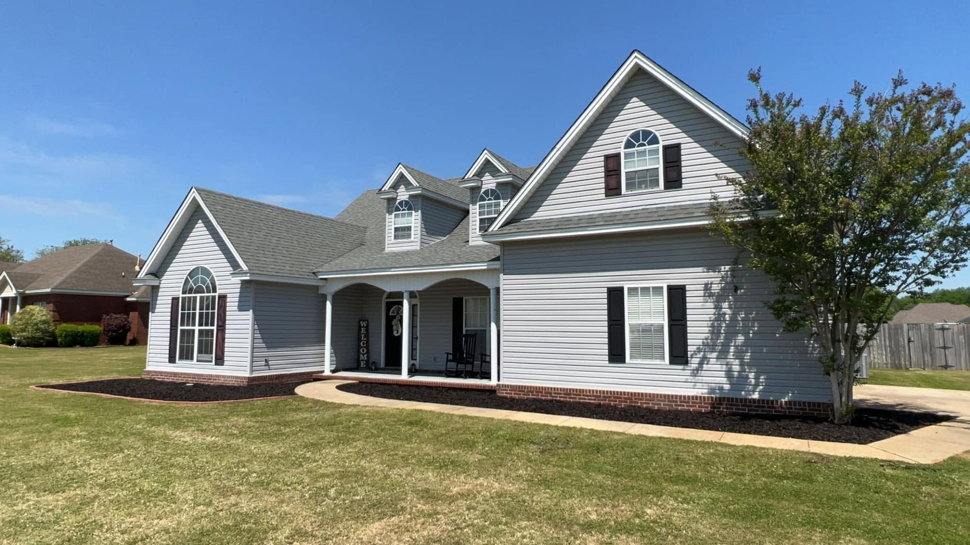 White suburban house with gray trim and front porch on a sunny lawn