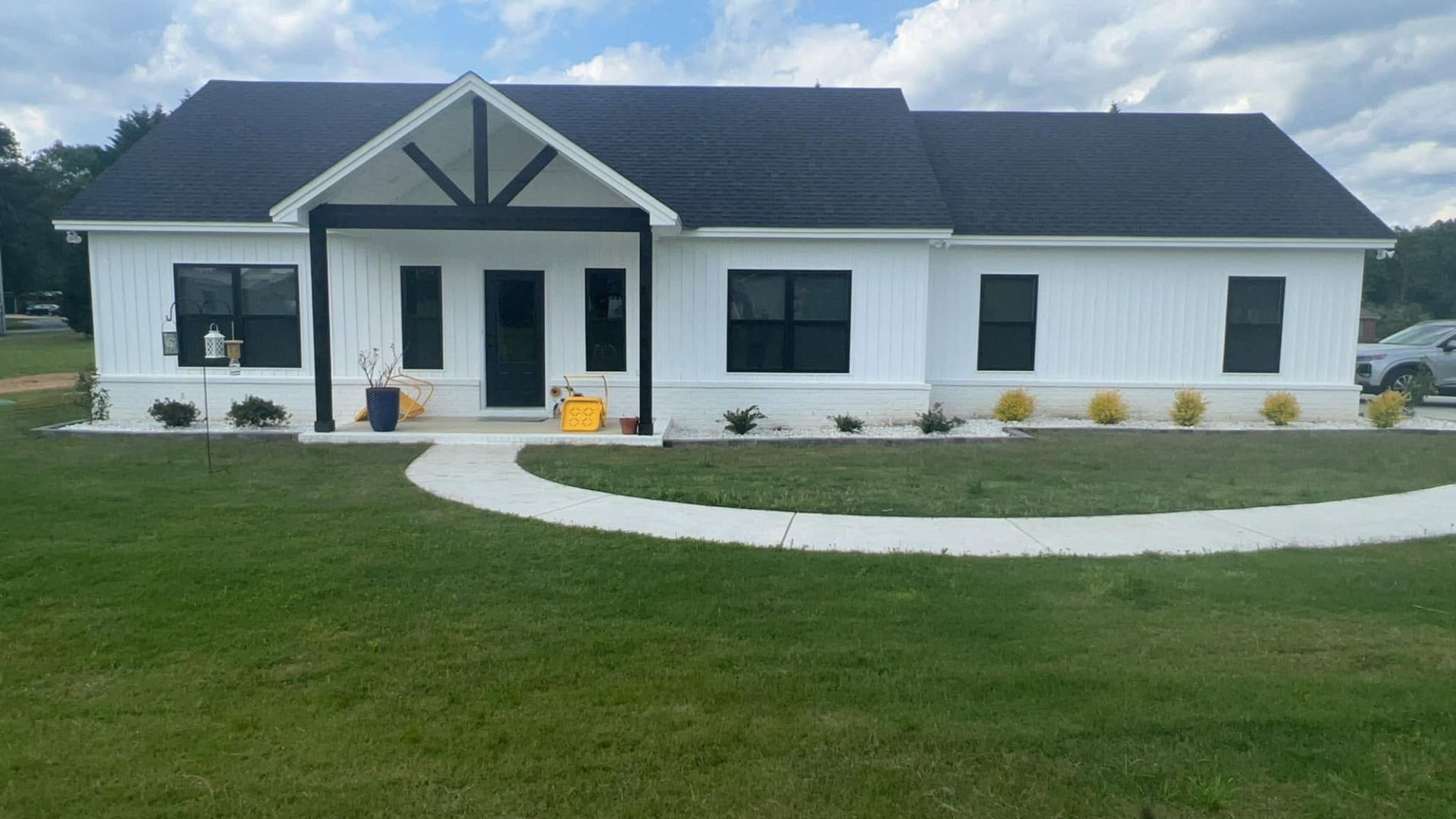 White single-story house with a black roof, front porch, and curved walkway in a green lawn.