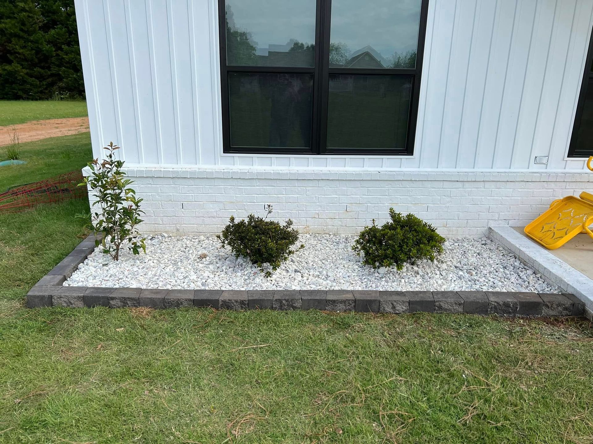 White house exterior with small garden bed, shrubs, and a yellow ramp on the right