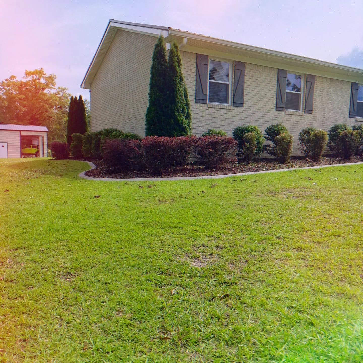 Suburban house with beige siding, green lawn, trimmed shrubs, and a garage in the background