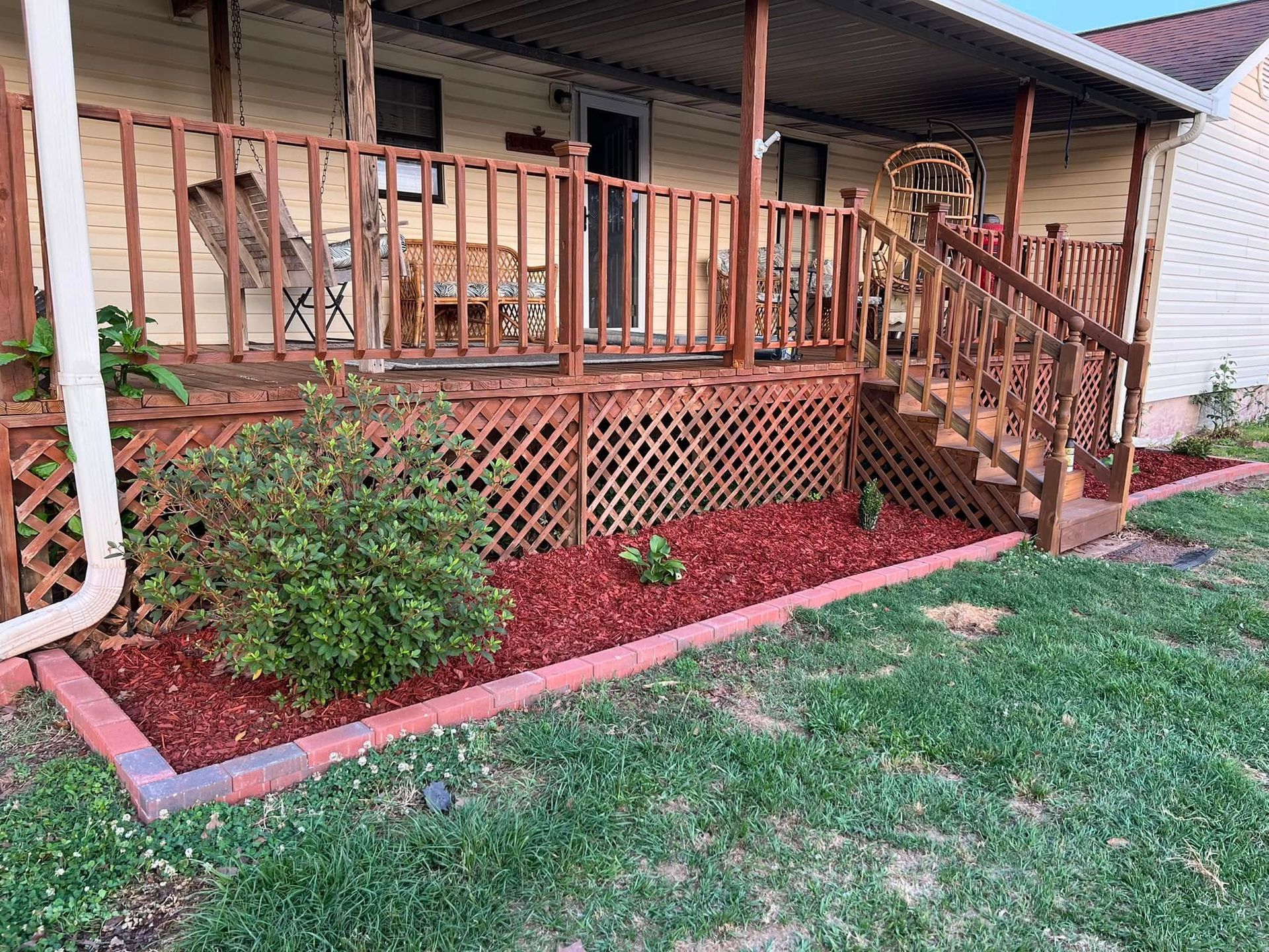 Wooden front porch with railings, steps, and a lattice skirt beside a grassy yard.