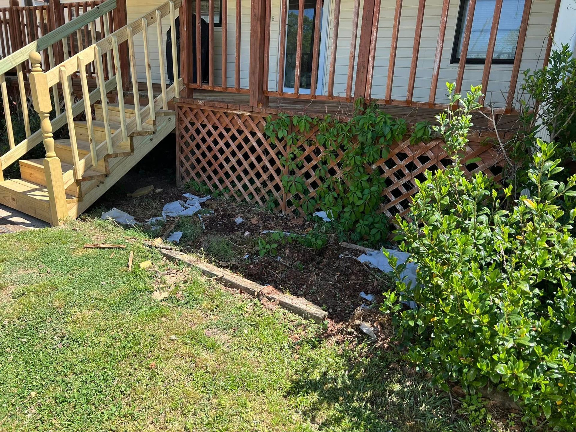 Backyard deck with wooden stairs, lattice skirting, and a small garden bed beside a grassy lawn