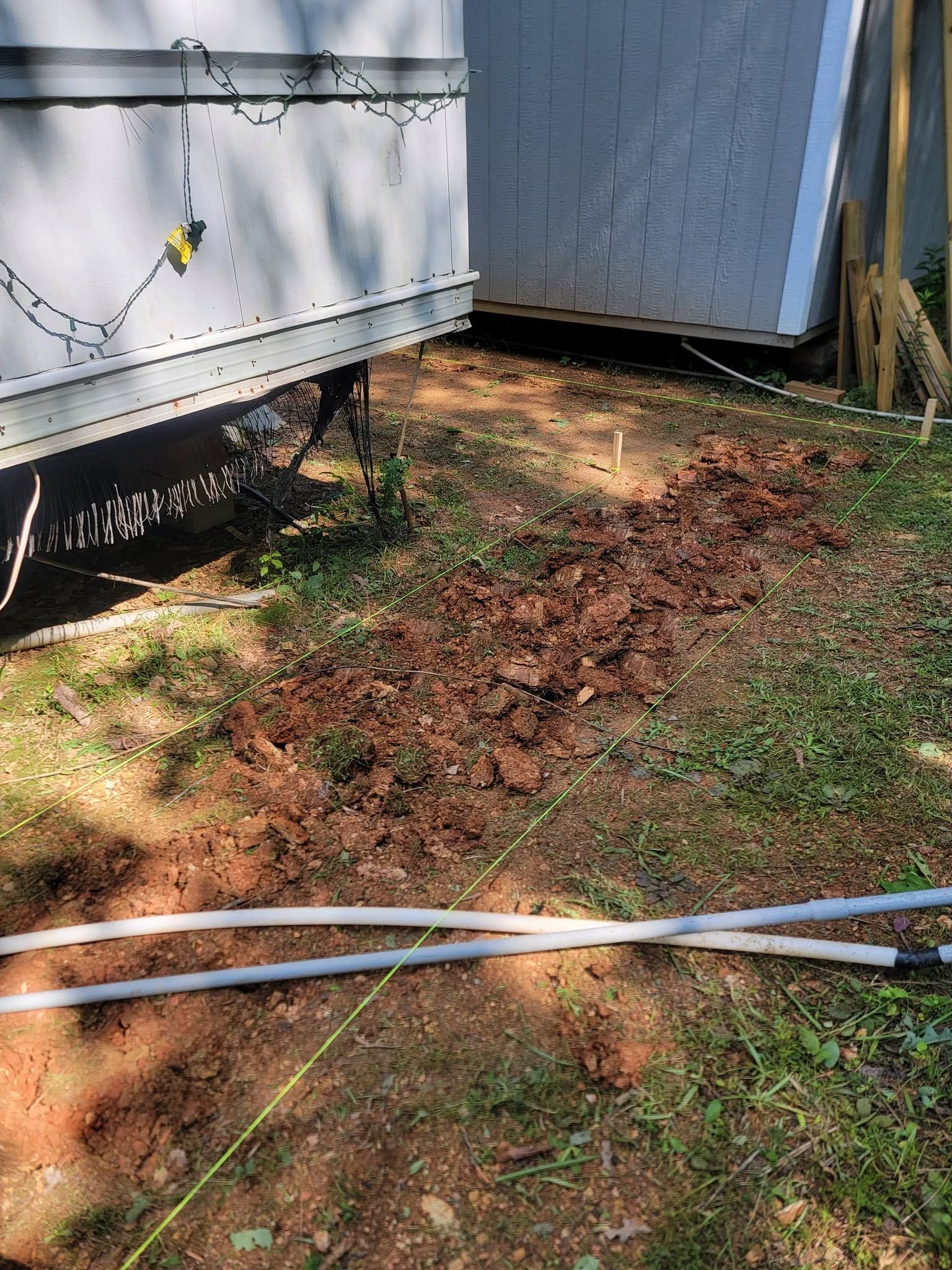 Two mobile homes beside a patchy yard with exposed soil, fallen leaves, and white hoses on the ground