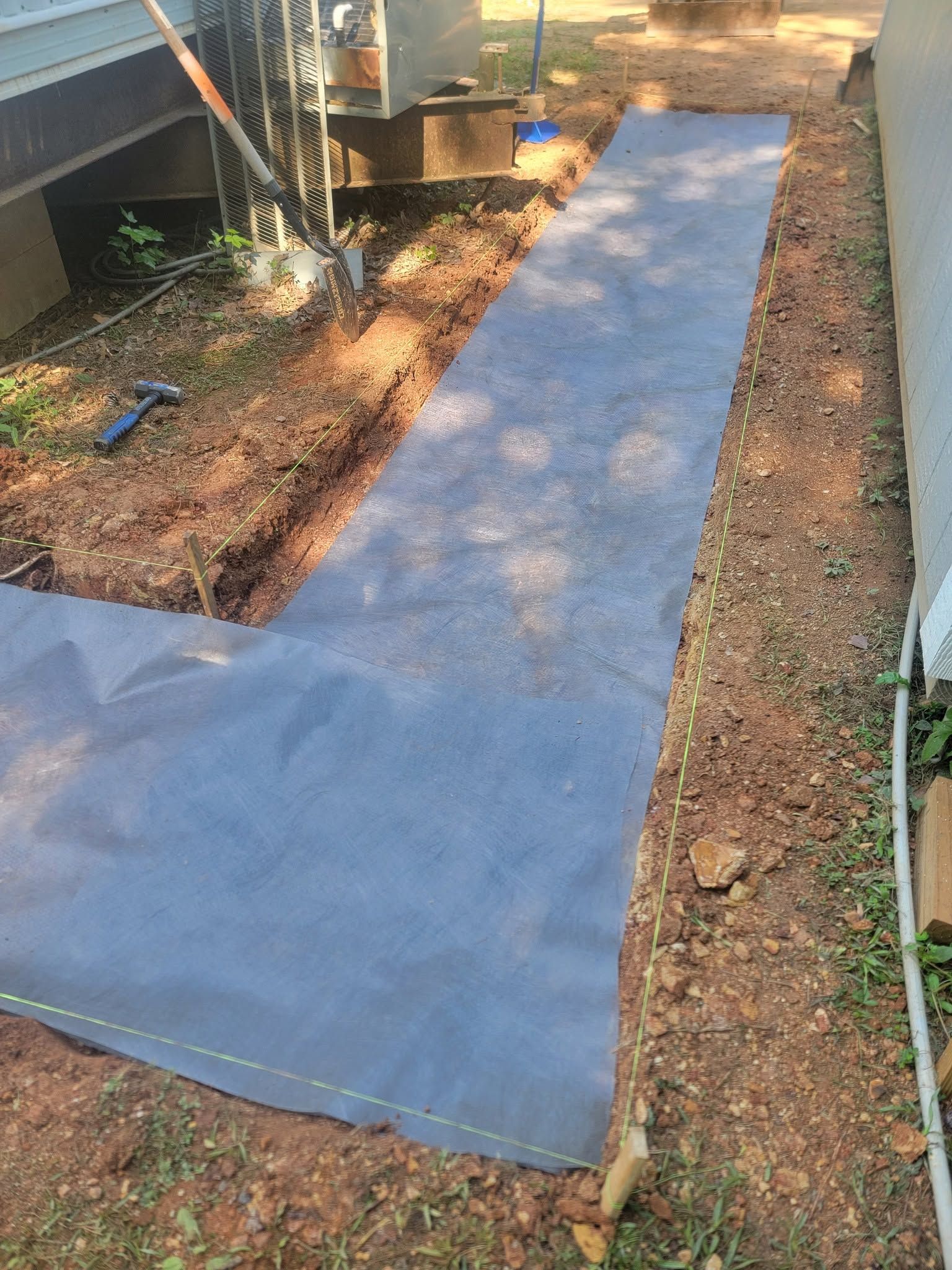 Black landscaping fabric laid over a narrow garden bed beside a house, with exposed soil edges.