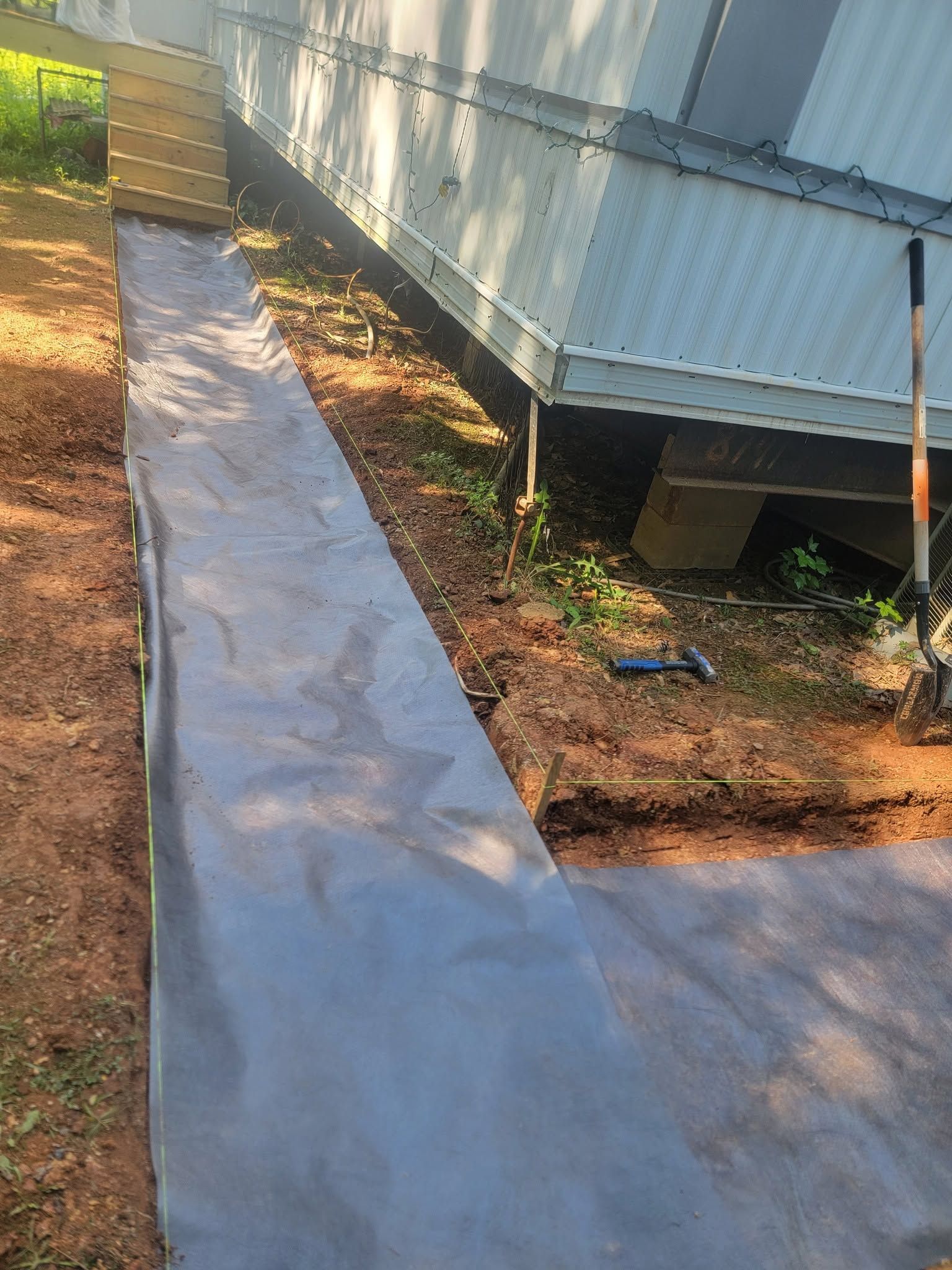 Concrete path beside a raised white mobile home, with dirt yard and sunlight.